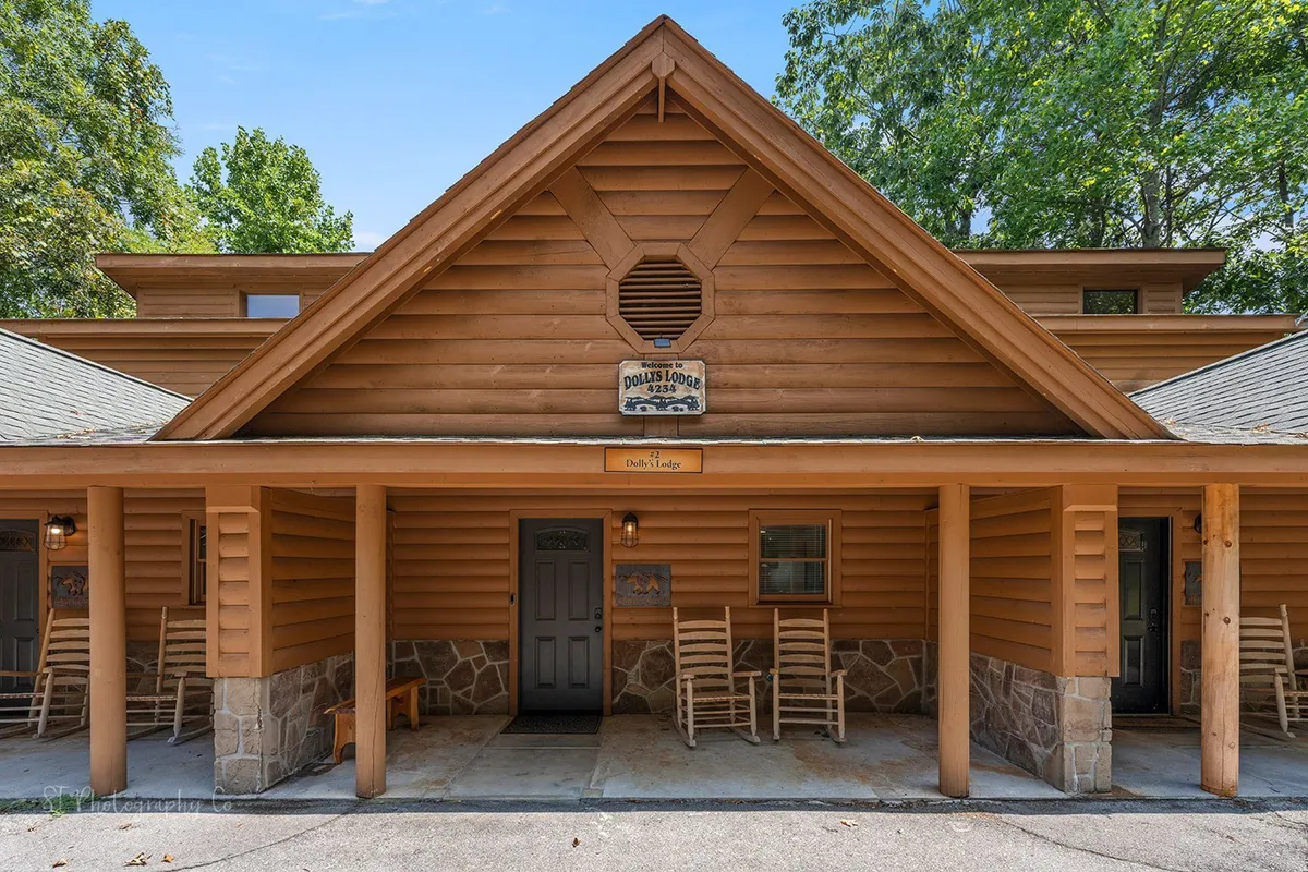 This exterior image features the wooden lodge facade, a welcoming stone foundation, and a porch equipped with rocking chairs and a lodge sign. The paved path and level entry are clearly visible, emphasizing easy arrival and accessibility.