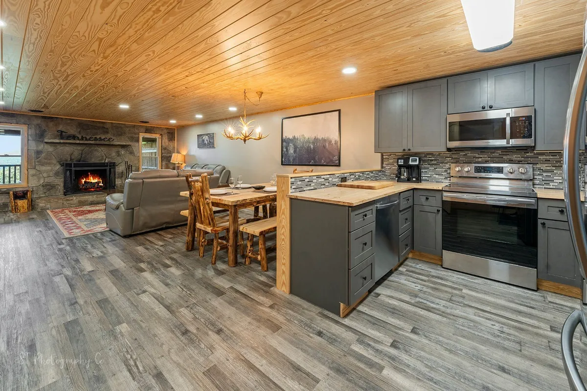 This image showcases a spacious, open-plan living area with a fireplace, inviting sofa, large dining table, kitchen island, and welcoming artwork. The scene is set for group relaxation, socializing, dining, and enjoying leisure time together.