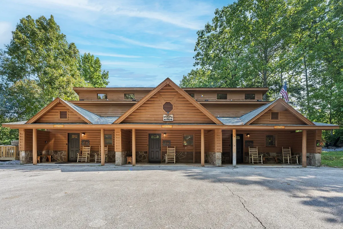 This image shows the log cabin structure from the exterior, with inviting rocking chairs placed on the porch and front doors visible. The setting is surrounded by natural greenery, suggesting a connection to the outdoors, and the porch creates a welcoming atmosphere for families returning from adventures.