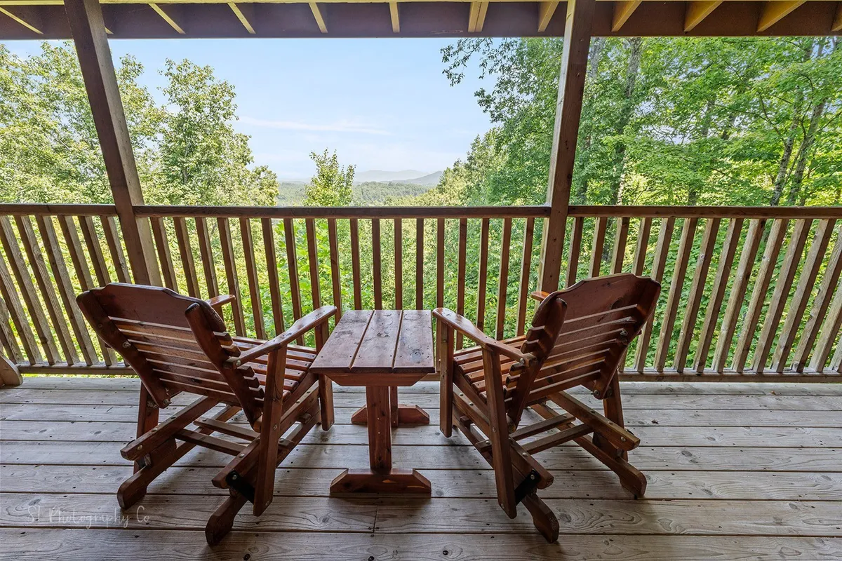 A covered outdoor area with multiple rocking chairs and a wooden table, overlooking distant mountains and encircled by rich green foliage. The space is perfect for gathering, sipping coffee, or simply unwinding in nature.