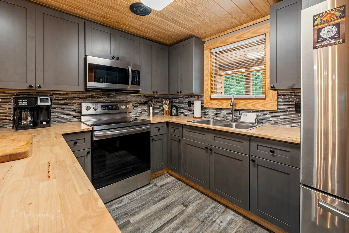 A sleek, fully equipped kitchen featuring stainless steel appliances, wooden countertops, a mosaic backsplash, and a window that brings in natural light. The space is modern yet inviting, designed for cooking family meals or baking treats together.
