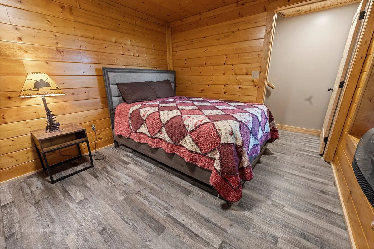 A beautifully made bed topped with a patchwork quilt, accompanied by a soft-glowing bedside lamp. The setting is tranquil and intimate, offering a sense of restful retreat surrounded by rustic decor, perfect for unwinding as a couple.